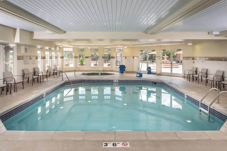 Indoor heated swimming pool with aqua water, comfortable seating, and bright natural light from windows