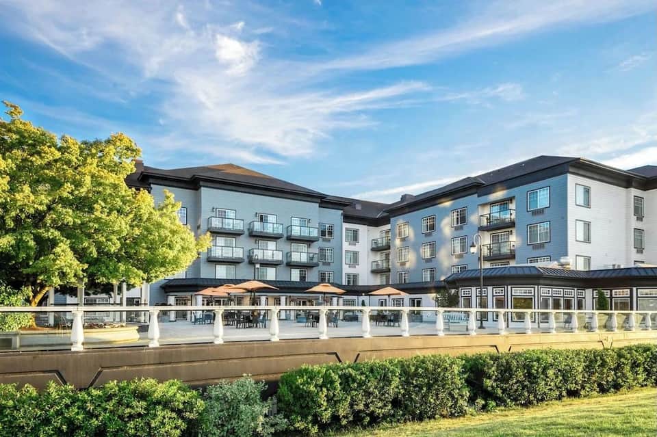 Riverside hotel exterior with waterfront patio, umbrellas, dining seating, and modern architecture