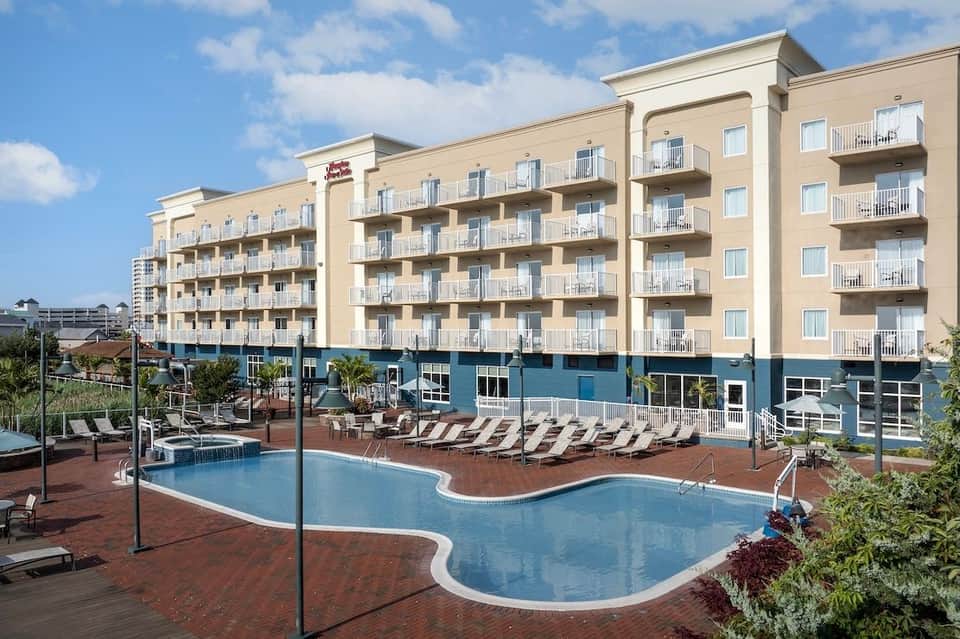 Beige hotel building with blue base and curved outdoor pool surrounded by lounge chairs
