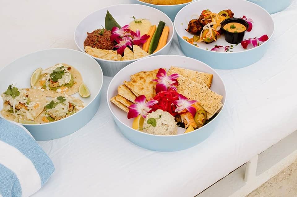 Four elegantly plated appetizers in light blue bowls garnished with pink flowers, lime, and fresh herbs