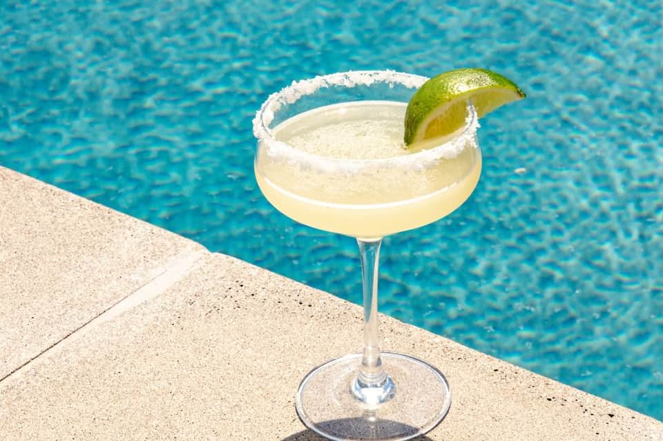 Margarita cocktail with salt rim and lime wedge positioned at edge of resort swimming pool