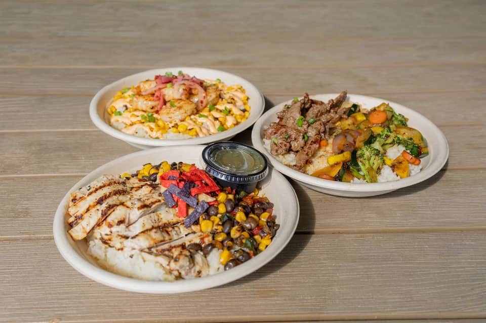 Three plated dishes featuring grilled proteins, roasted vegetables, and rice on wooden surface