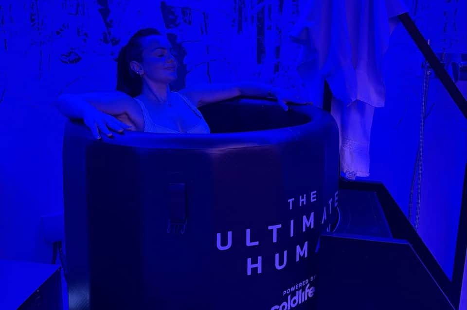 Woman in spa pod receiving cold water treatment in blue-lit wellness chamber facility