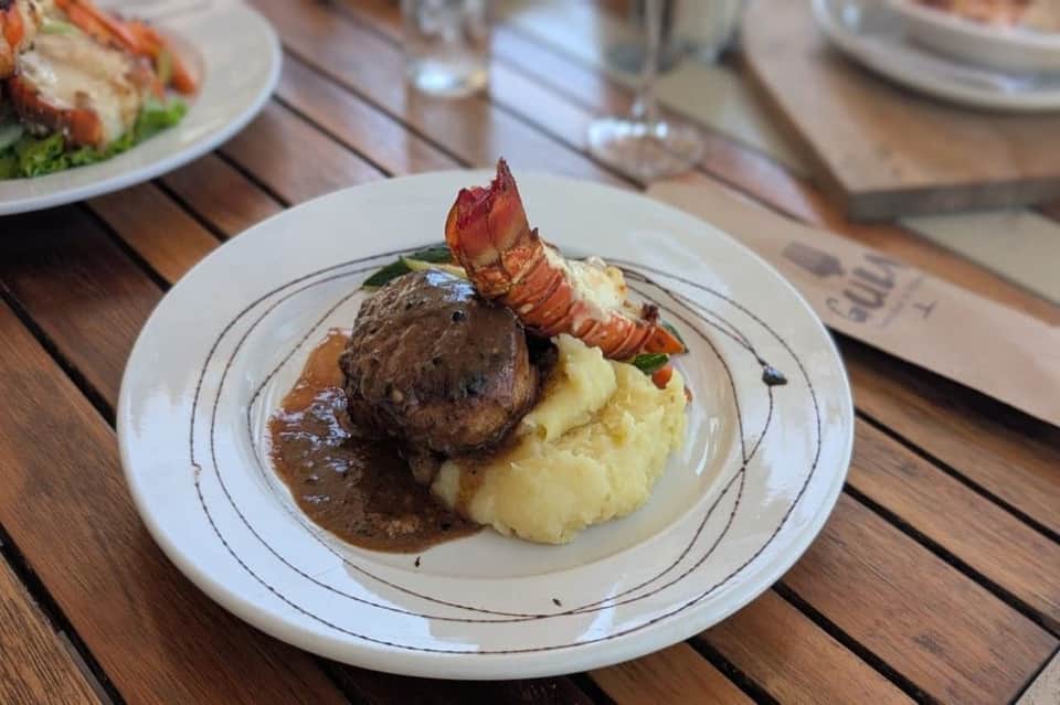 Filet mignon with lobster tail, mashed potatoes, and brown sauce on white plate