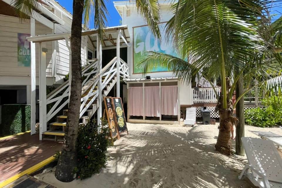 Beach resort walkway with white wooden structures, palm trees, and sandy pathways