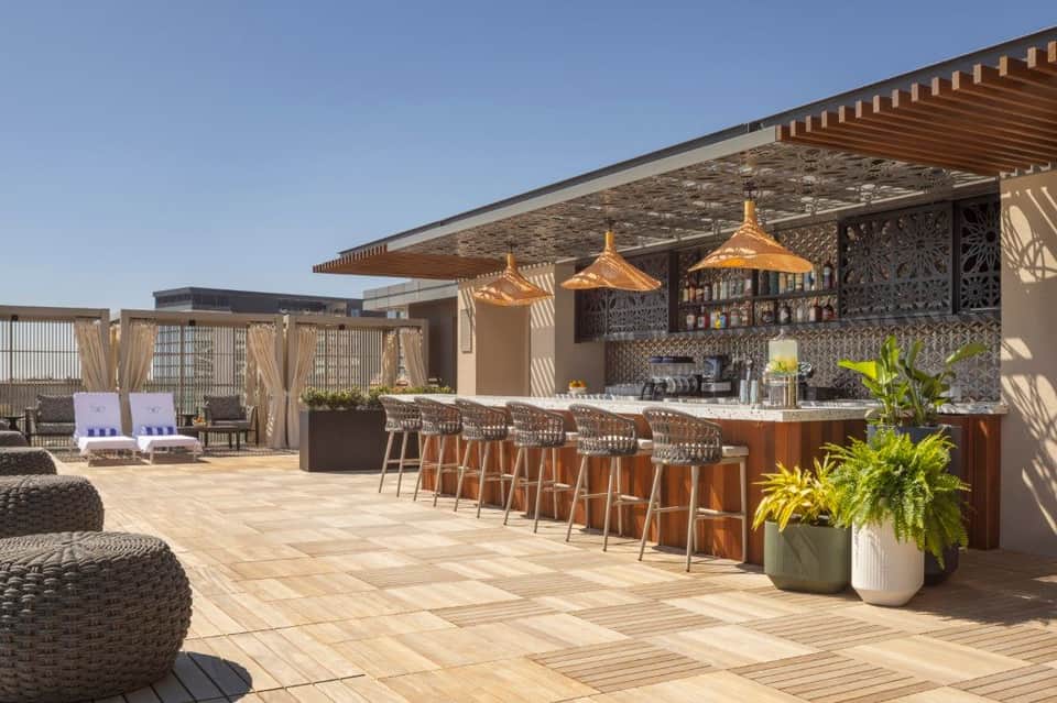 Modern rooftop bar with woven pendant lights, wooden pergola, and desert-inspired seating areas
