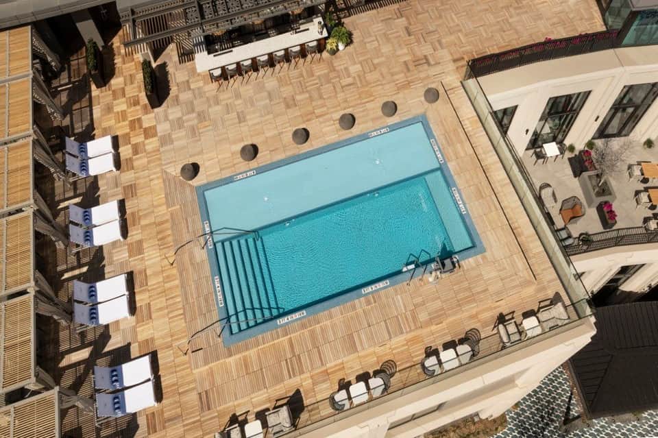 Aerial view of resort pool surrounded by wooden deck, lounge chairs, and multi-level terraces