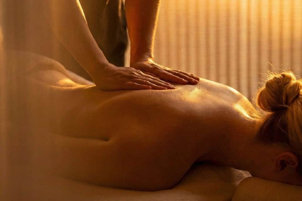 Spa massage therapy with therapist performing back massage on client in golden sunlight
