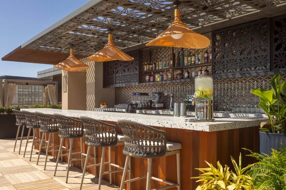 Upscale outdoor bar with woven pendant lights, patterned screens, and marble counter seating