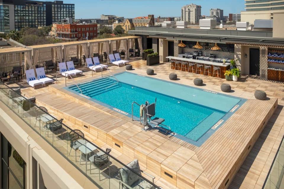 Rooftop pool deck with blue swimming pool, loungers with blue cushions, and city skyline views
