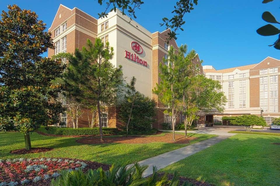 Hilton hotel grounds with brick building, manicured lawn, flowering landscaping, and trees