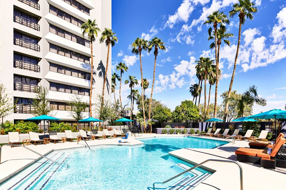 Resort pool area with turquoise water, lounge chairs, umbrellas, and tall palm trees