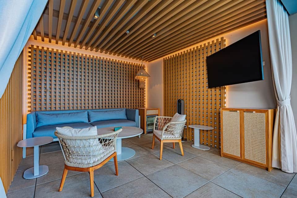 Modern lounge area with wooden slat walls, blue sofa, white chairs, and overhead linear ceiling design