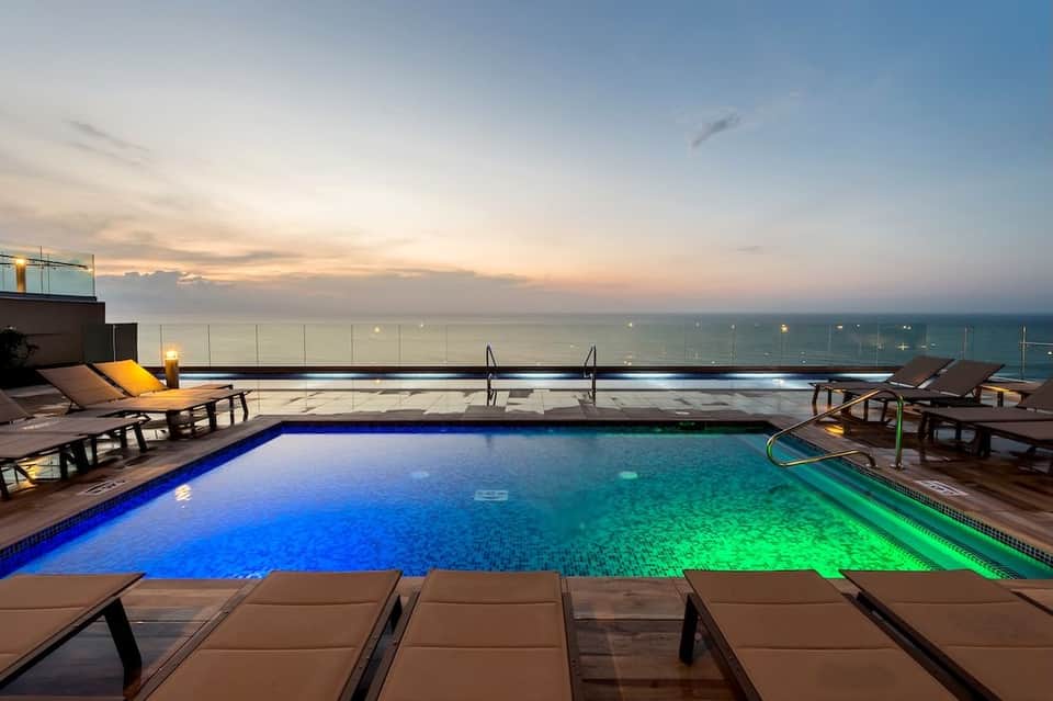 Rooftop infinity pool illuminated at dusk with ocean view and lounge chairs