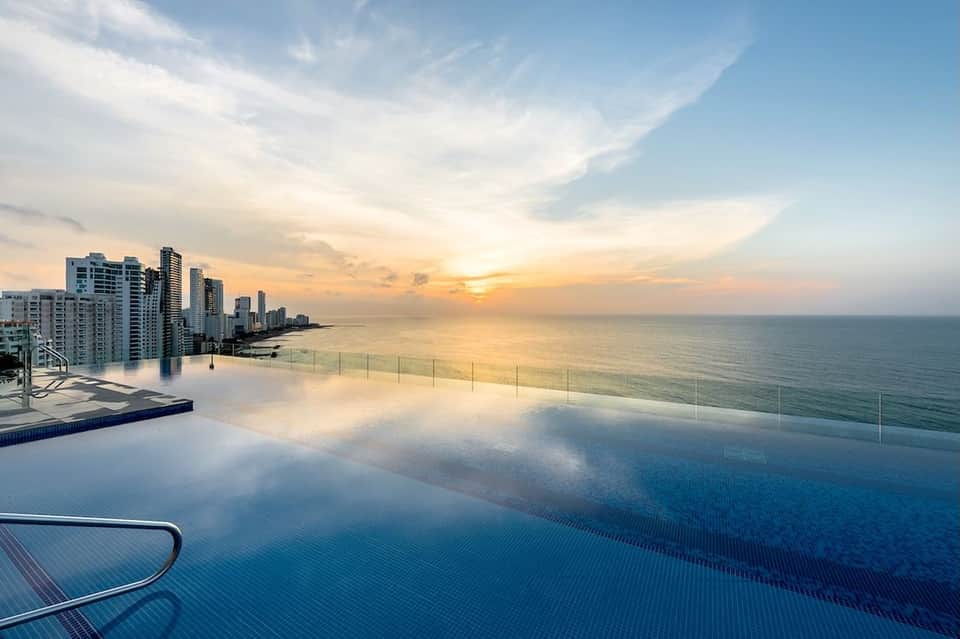 Infinity pool reflecting sunset sky with coastal city skyline and glass railings