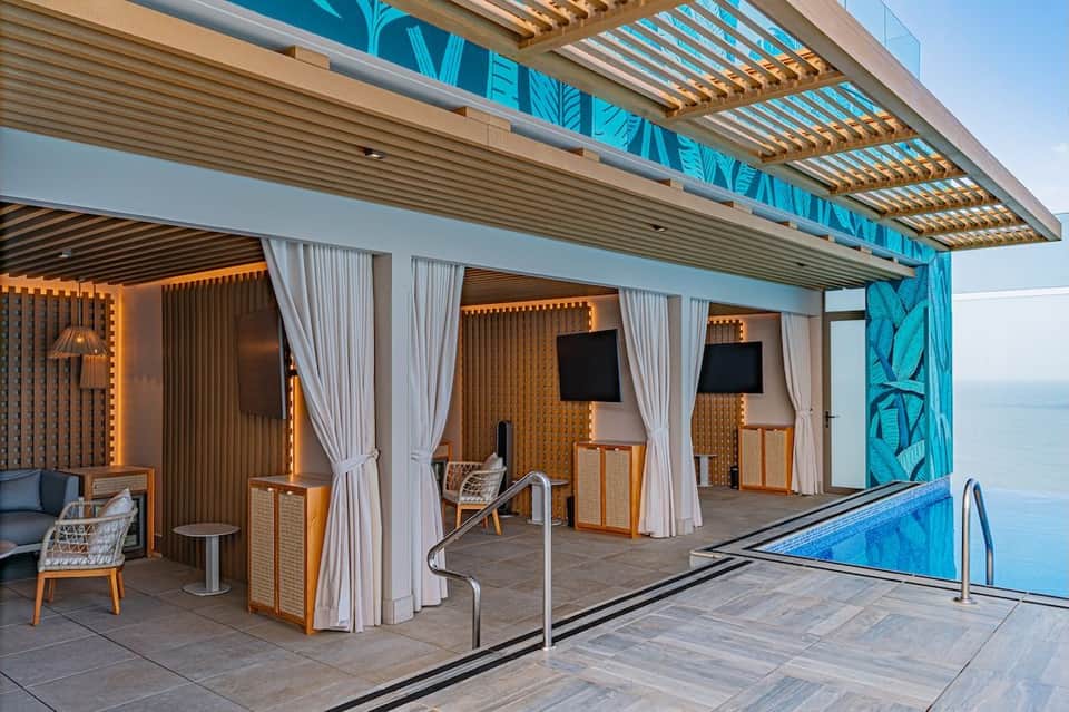 Poolside lounge area with wooden pergola, white curtains, and ocean views