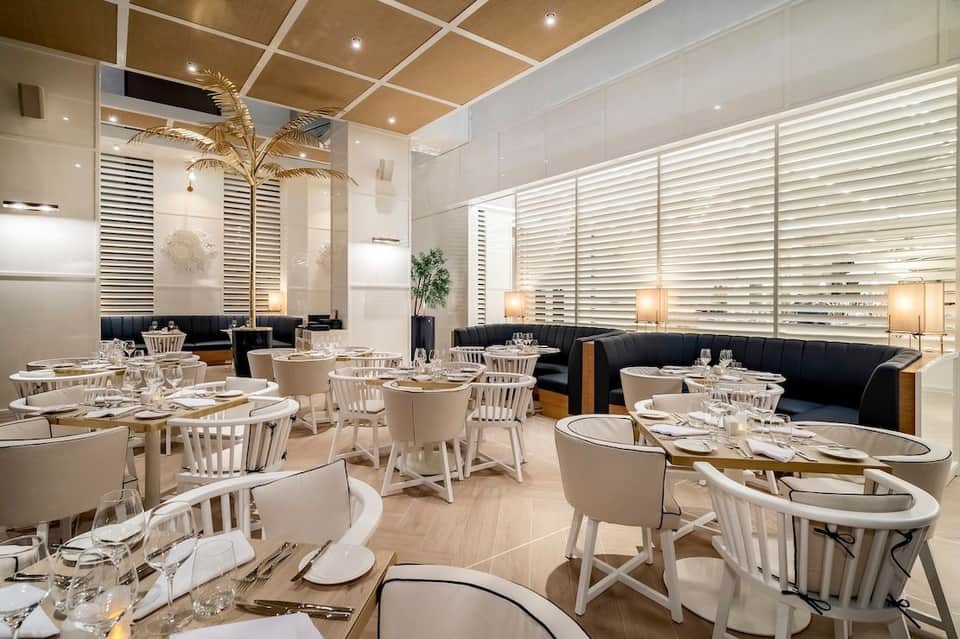 Modern restaurant dining room with white chairs, round tables, and geometric wall design
