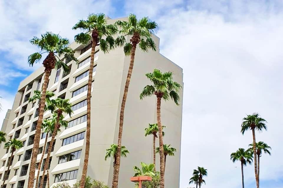 Beige mid-rise hotel building with tall palm trees against blue sky