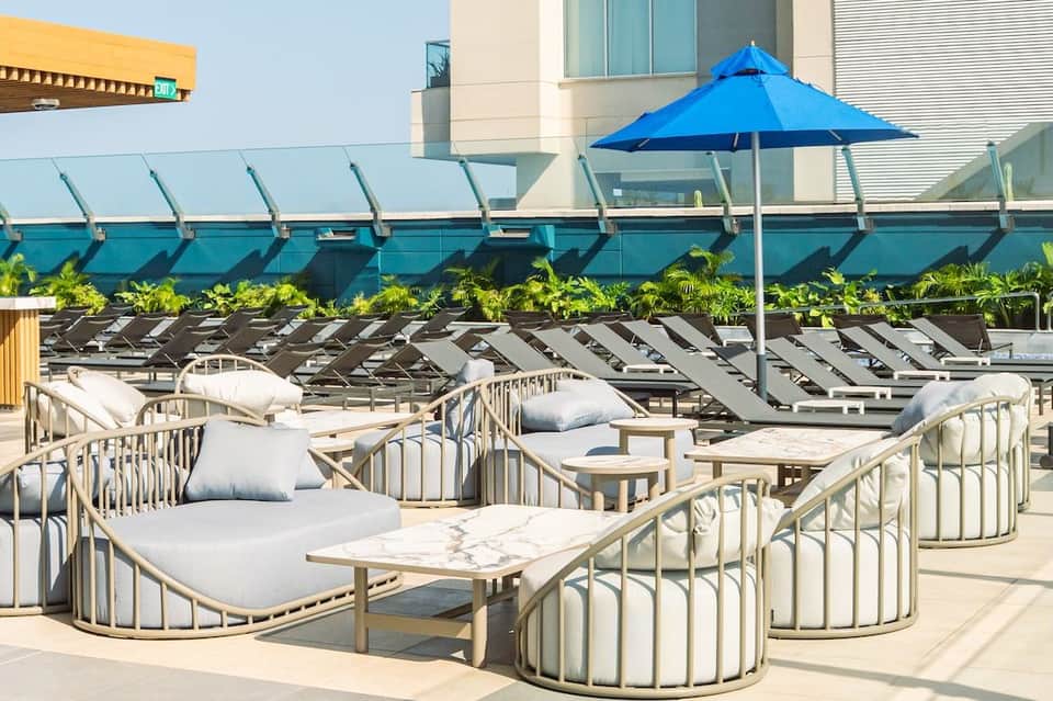 Rooftop lounge area with curved seating pods, white cushions, blue umbrella, and city views