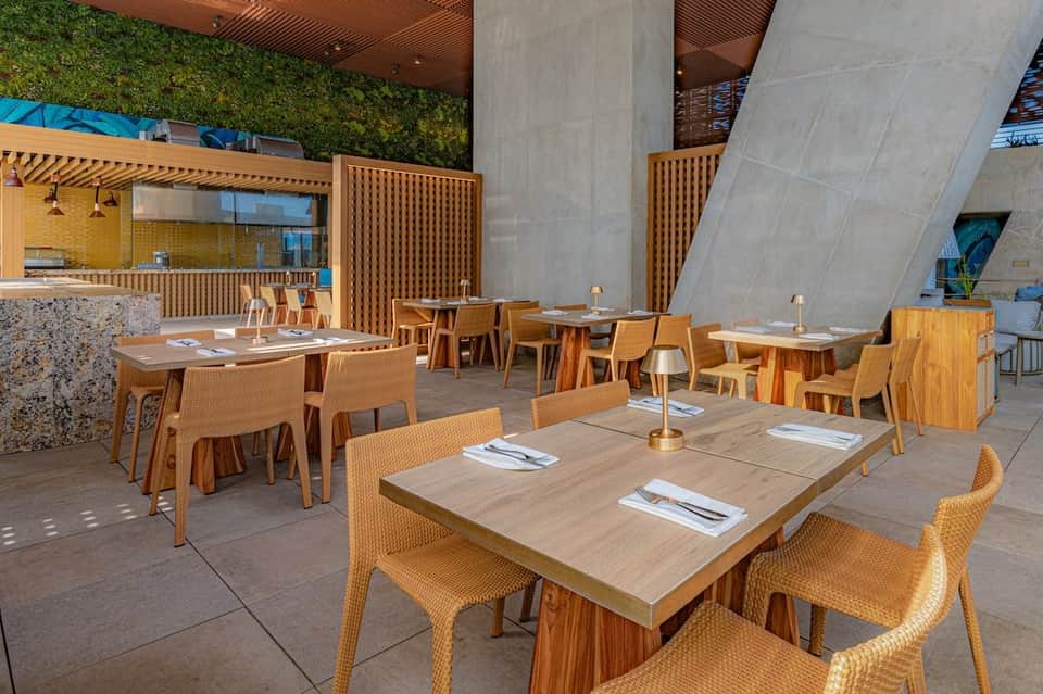 Modern outdoor dining space with wooden tables, rattan chairs, concrete pillars, and green wall