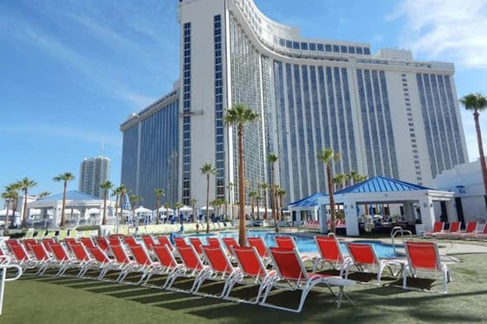 Resort pool with red lounge chairs, palm trees, white gazebo, and large curved hotel building