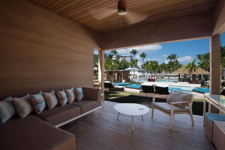 Modern resort cabana interior with brown sofa, wood ceiling, and pool view through opening