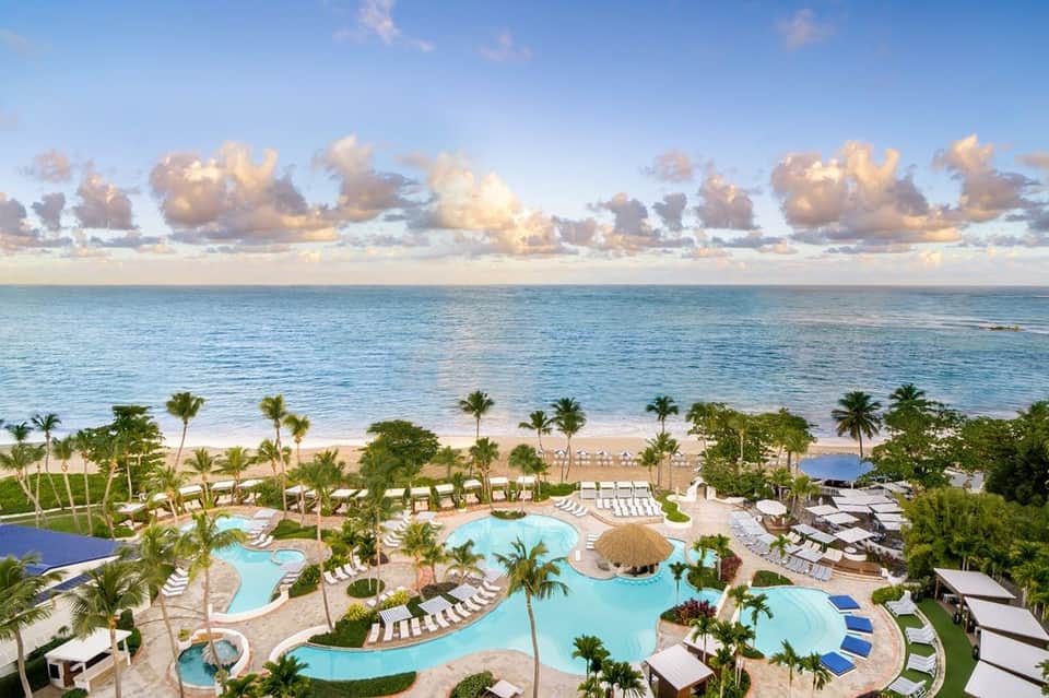 Aerial view of beachfront resort with multiple pools, palm trees, and turquoise ocean
