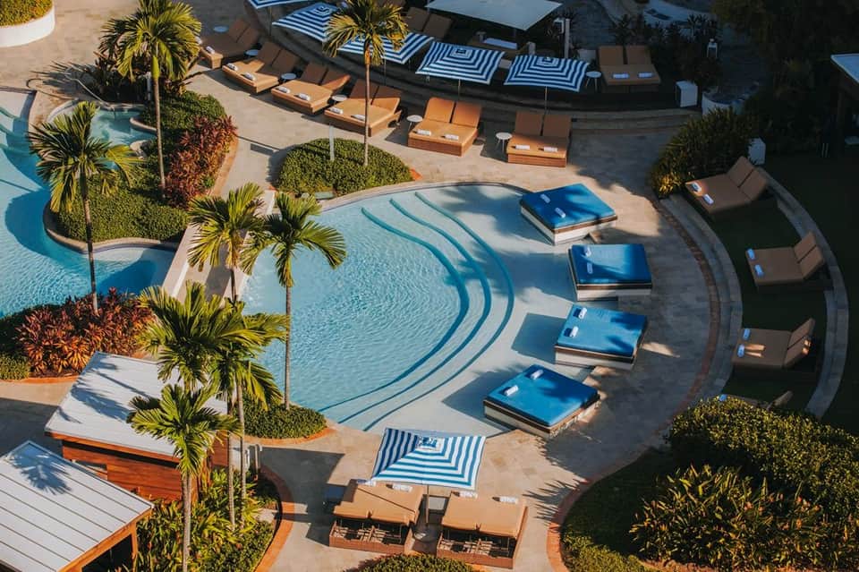 Overhead view of curved resort pool with blue loungers, orange seating areas, and palm trees