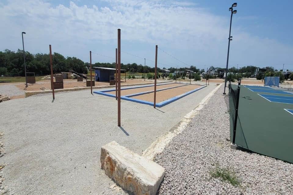 Outdoor recreation area with volleyball courts, pickleball courts, and fitness equipment on sandy ground