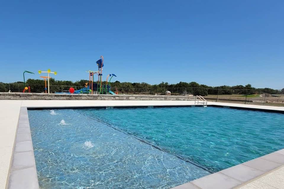 Resort swimming pool with water slide and playground structure visible in background under clear sky