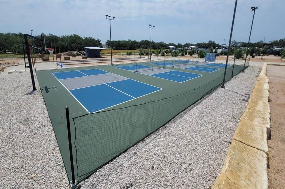 Multiple pickleball courts with blue and green surfaces, fencing, and tall light poles