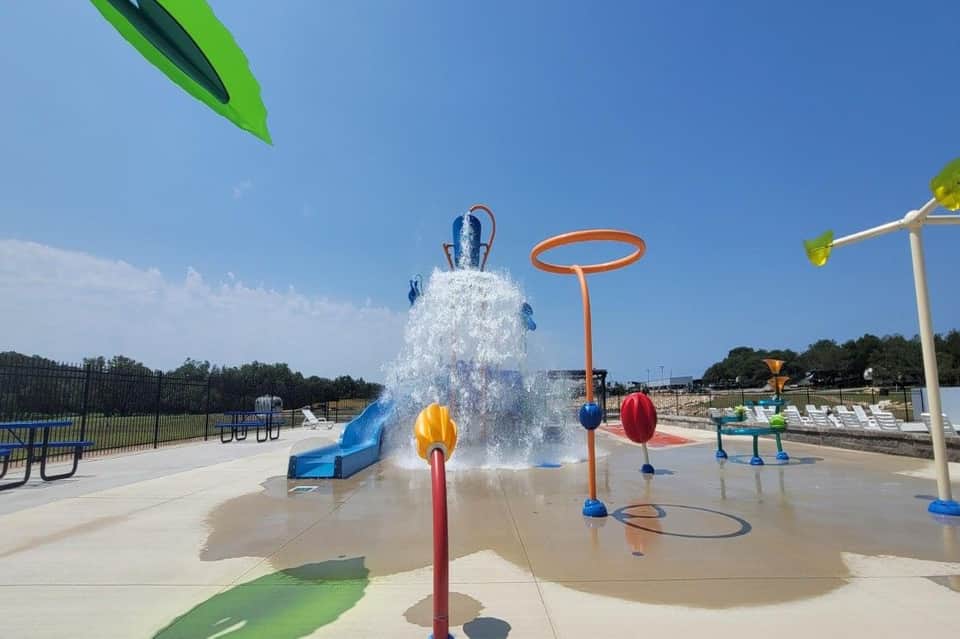 Splash pad water play area with bucket pour feature, water jets, and colorful interactive elements