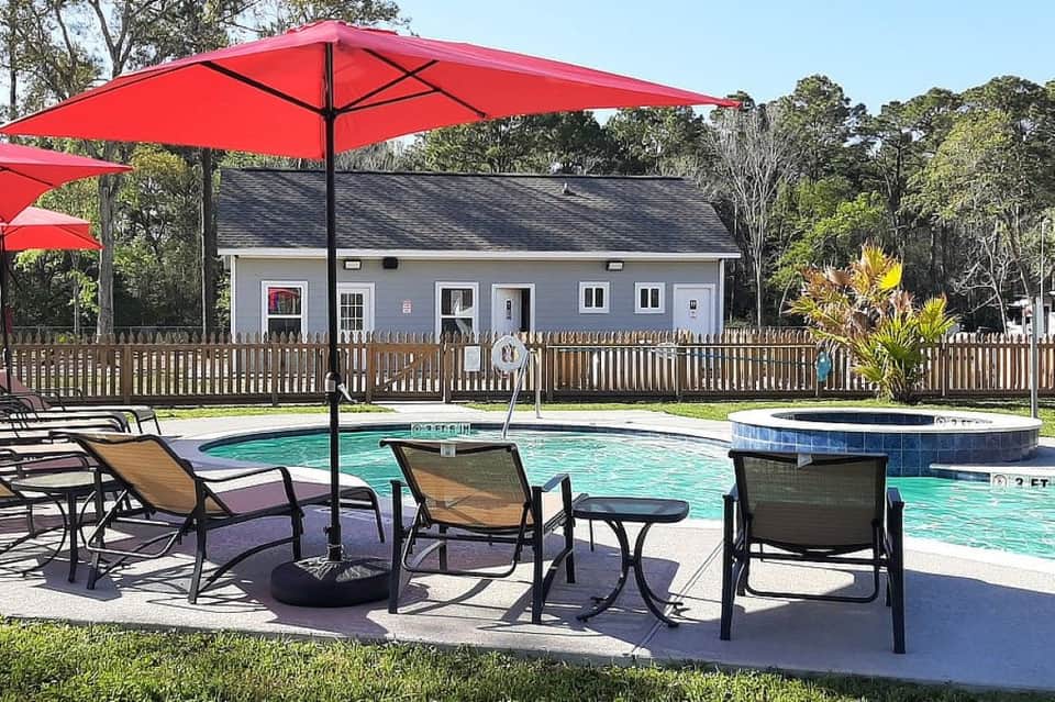 Resort pool area with lounge chairs, red umbrellas, spa hot tub, modern building, and manicured grounds