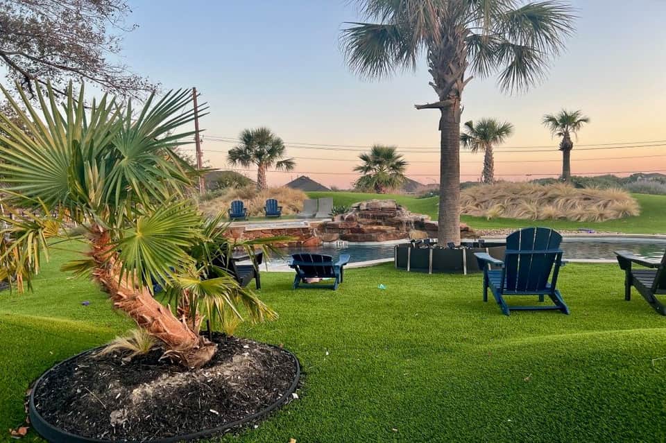 Waterfront property with Adirondack chairs, palm tree, fire pit, dock, and peaceful sunset views