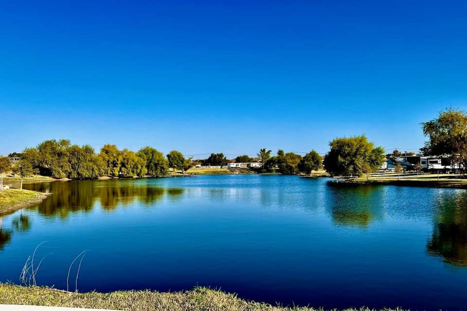 Scenic lake view with clear blue water, grassy shoreline, trees, and residential community waterfront