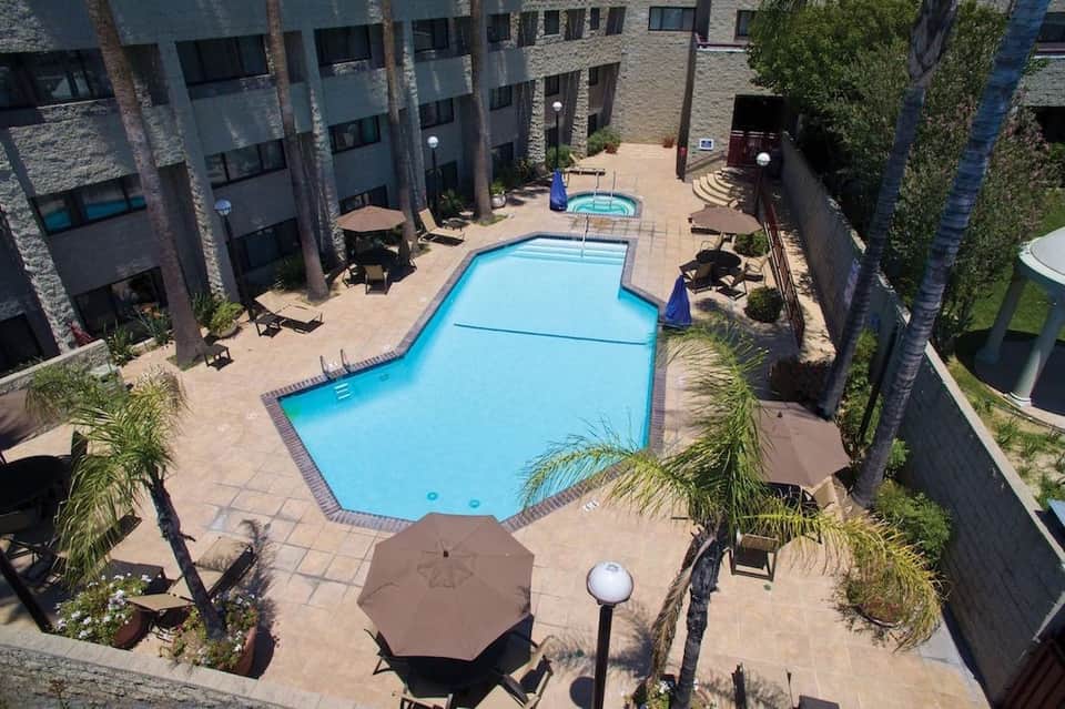 Aerial view of hotel pool courtyard with blue lap pool, surrounding buildings, palm trees, and terrace seating areas