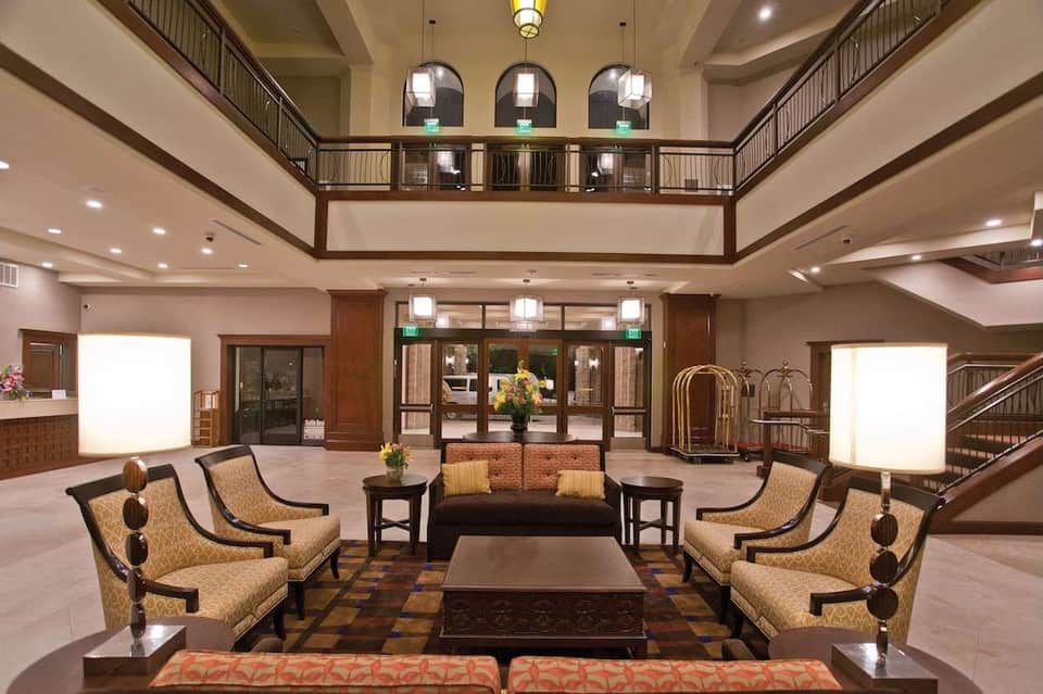 Elegant hotel lobby with high ceilings, two-story balcony, gold-patterned upholstered chairs, and central seating arrangement