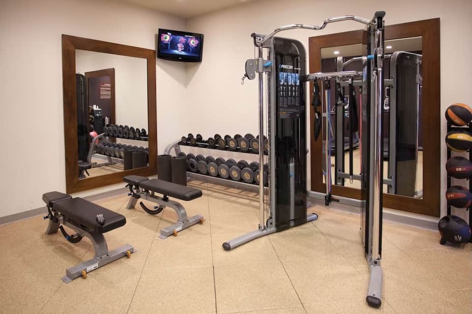 Modern fitness center with dumbbells, weight machines, mirrors, and cardio equipment