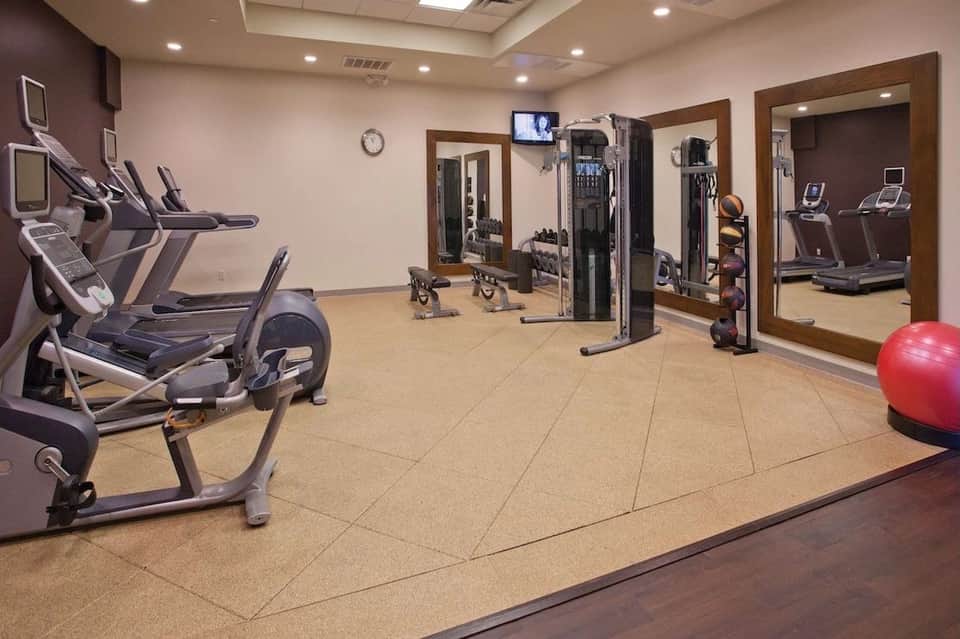 Bright fitness facility with cardio machines, exercise bike, weight equipment, and mirrors