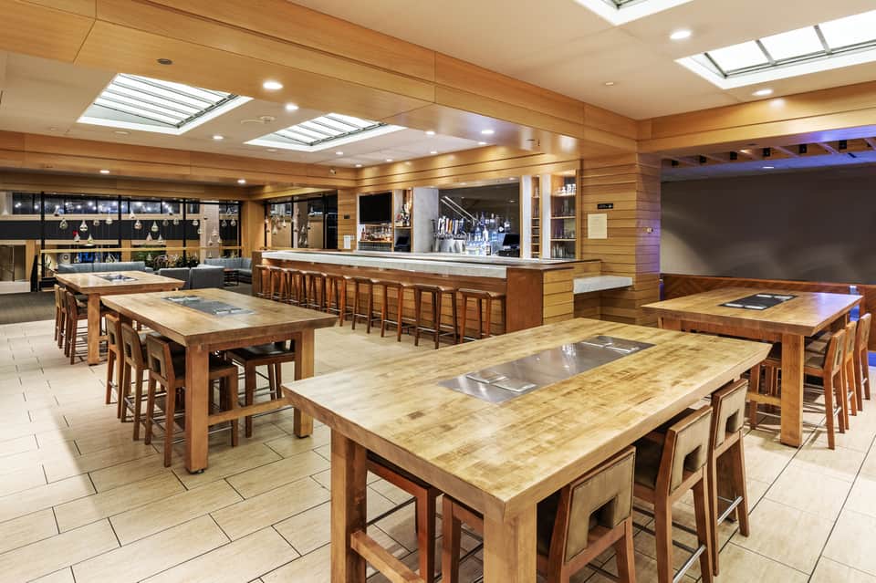 Modern culinary kitchen with wooden tables, chef stations, bar seating, and skylight ceiling