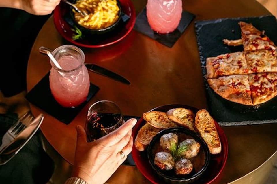 Overhead view of dinner table with cocktails, pizza, and appetizers
