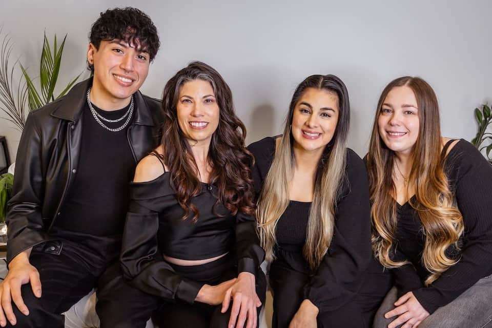 Four young adults posing together wearing black outfits against white wall