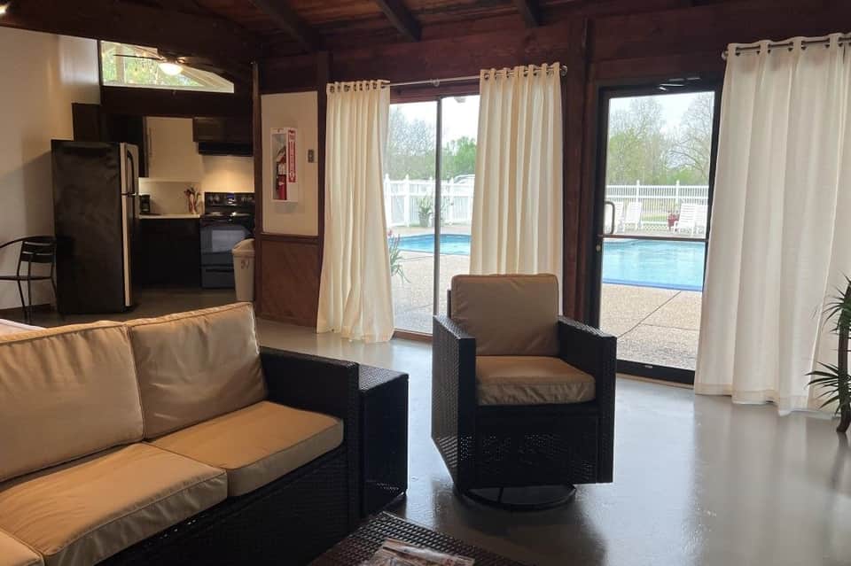 Resort lounge interior with brown furniture, full kitchen, glass doors overlooking pool and patio