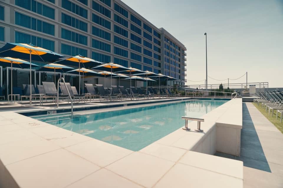 Resort pool deck with yellow umbrellas, lounge chairs, modern hotel building, and city skyline views