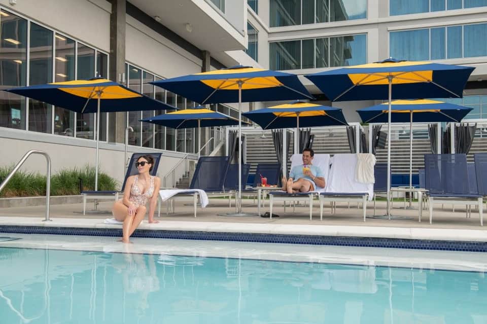 Resort pool with blue and yellow umbrellas, lounge chairs, and modern building facade on sunny day