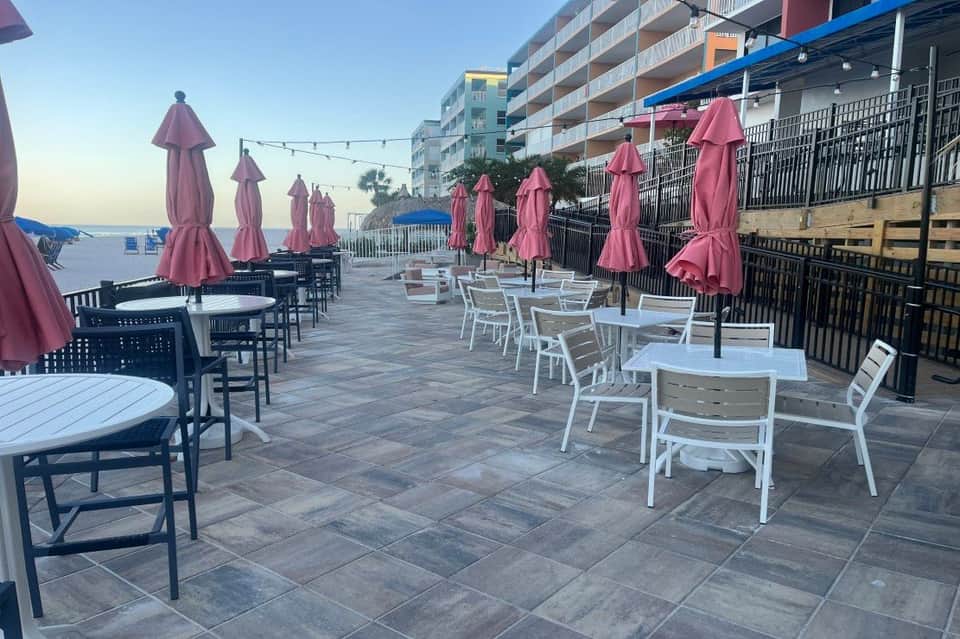 Beachfront terrace with pink umbrellas, white furniture, string lights, and multi-story hotel building