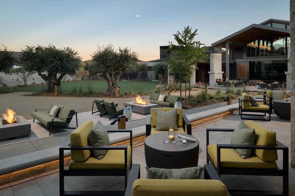 Upscale outdoor lounge at dusk with fire pits, seating groups, and modern building architecture