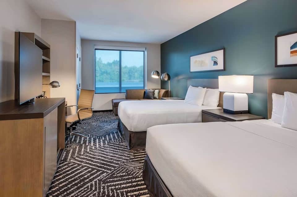 Double queen hotel room with teal walls, waterfront view windows, work desk, and contemporary furnishings