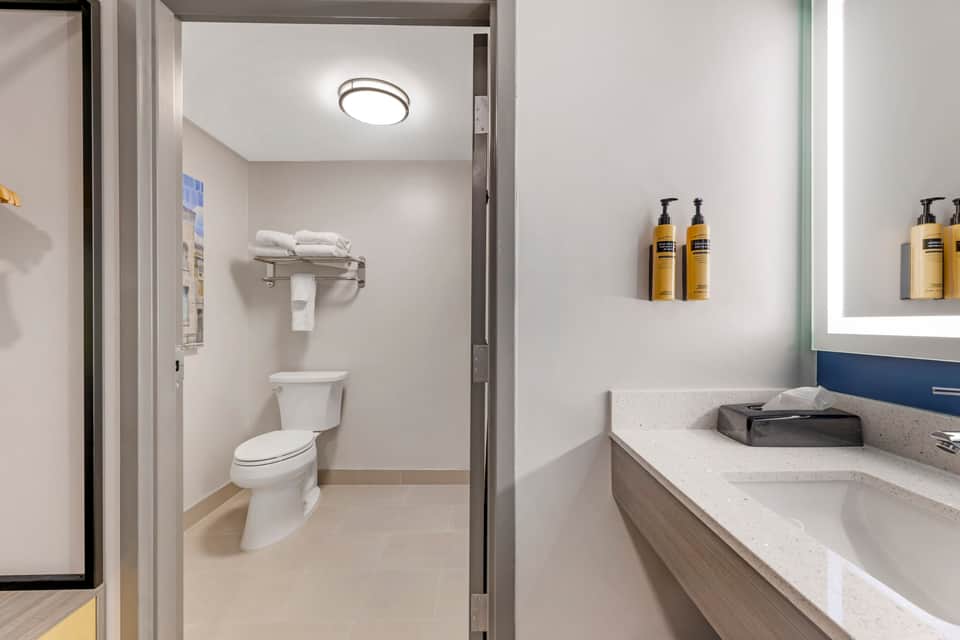 Clean bathroom vanity with sink, mirror, toiletries, and adjacent toilet in hotel room