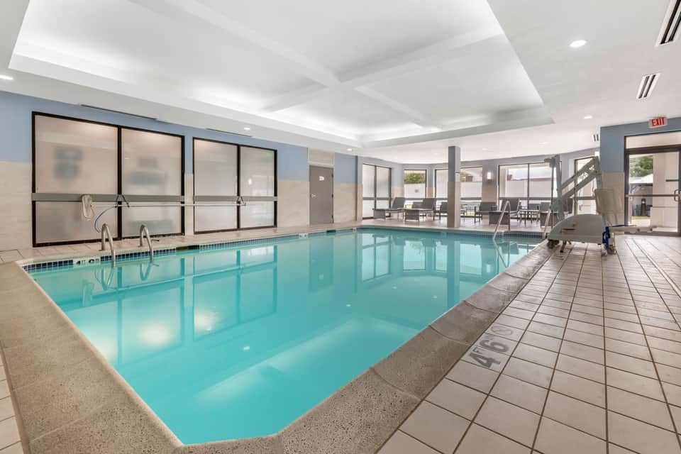 Indoor heated saltwater pool with large windows, white coffered ceiling, and ocean view access